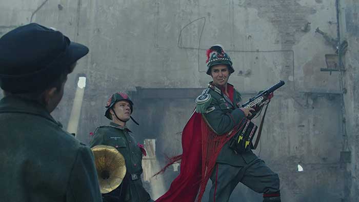 映画『ジョジョ・ラビット』より 右:クレンツェンドルフ大尉（サム・ロックウェル）が衣装替えして、戦場でジョジョに笑顔を送るシーン。